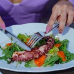 Woman enjoying an octopus salad with fresh greens outdoors. Vibrant and appetizing.