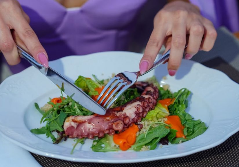 Woman enjoying an octopus salad with fresh greens outdoors. Vibrant and appetizing.